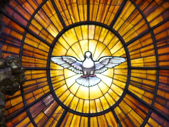 Stained glass window with a dove in the center, surrounded by warm colors.