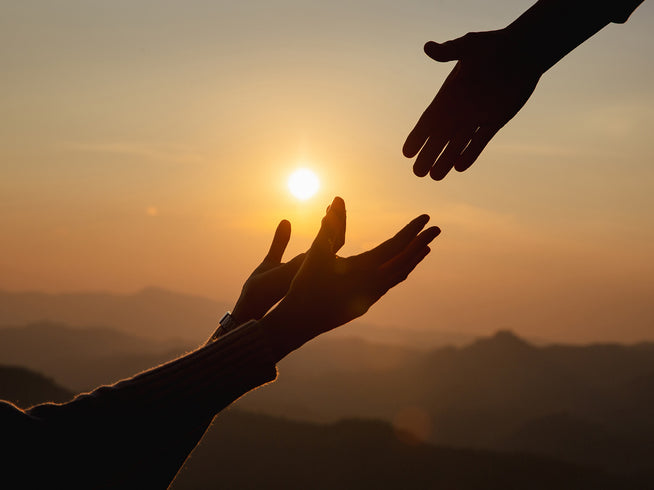 Two pairs of hands reaching towards each other with a sunset in the background