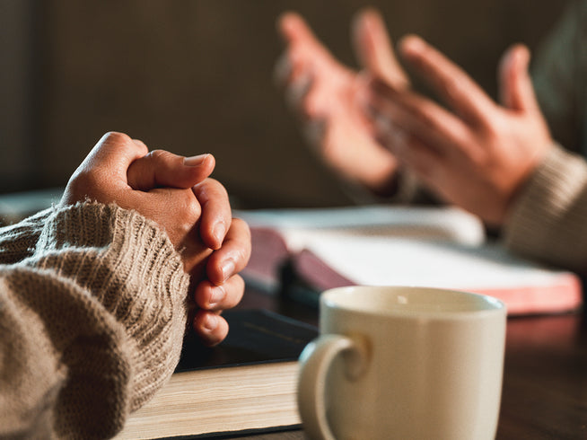 Two people holding hands across a table with a cup of coffee in the foreground.