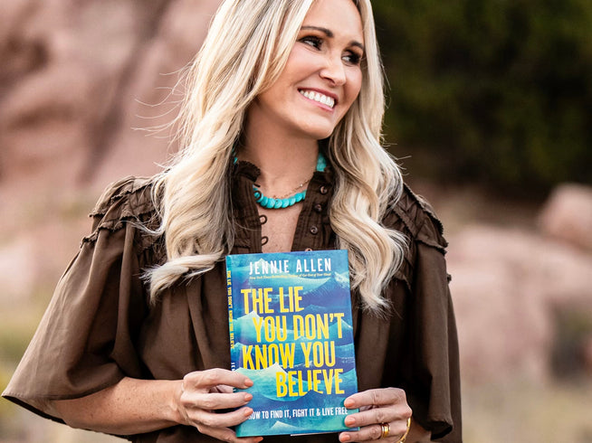 Woman holding a book titled 'The Lie You Don't Know You Believe' by Jennie Allen outdoors.