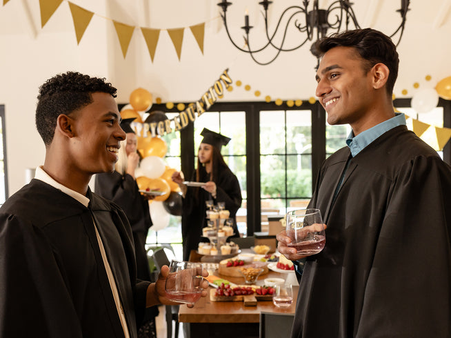 Two graduates in caps and gowns celebrating with drinks in a decorated room.