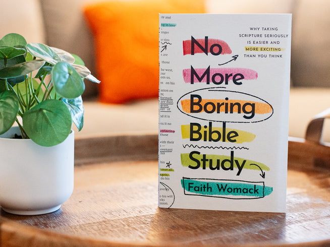 Book titled 'No More Boring Bible Study' by Faith Womack on a wooden surface with a plant and orange pillow in the background.