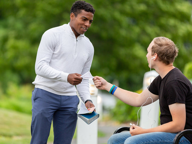 Two men interacting outdoors with a blurred green background