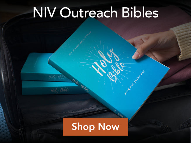 A hand placing a bright blue NIV Outreach Bible into an open suitcase, with two matching blue Bibles stacked inside. White text at the top reads 'NIV Outreach Bibles' and an orange 'Shop Now' button appears at the bottom.