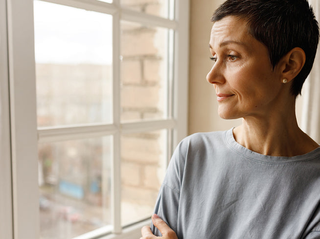 Woman standing by a window, looking outwards.