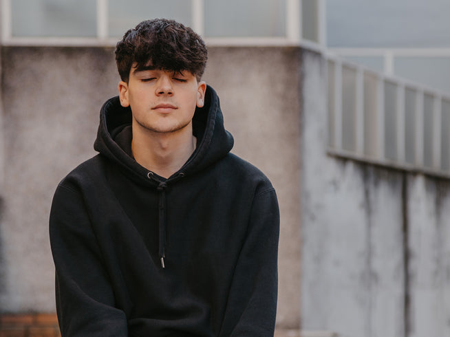 Person wearing a black hoodie sitting against a neutral background