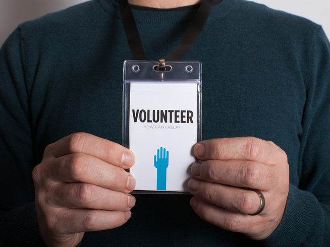 Person holding a volunteer badge with a hand icon and text.