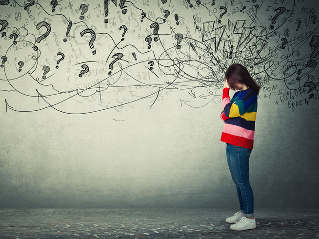 Woman in front of graffiti on a wall, with her head in her hands because she is worried