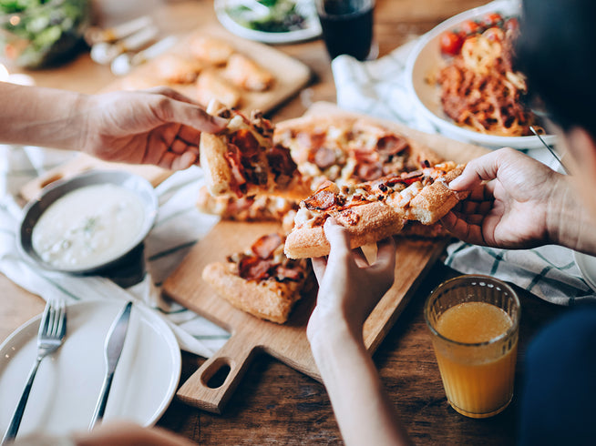 Image of a table with a pizza, a group of people are sharing the food