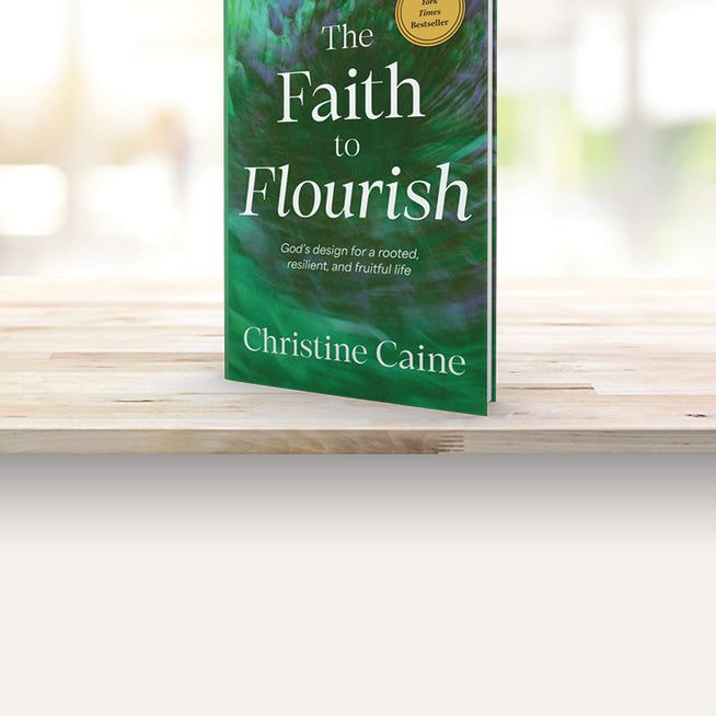 Book titled 'The Faith to Flourish' by Christine Caine on a wooden surface with a blurred background