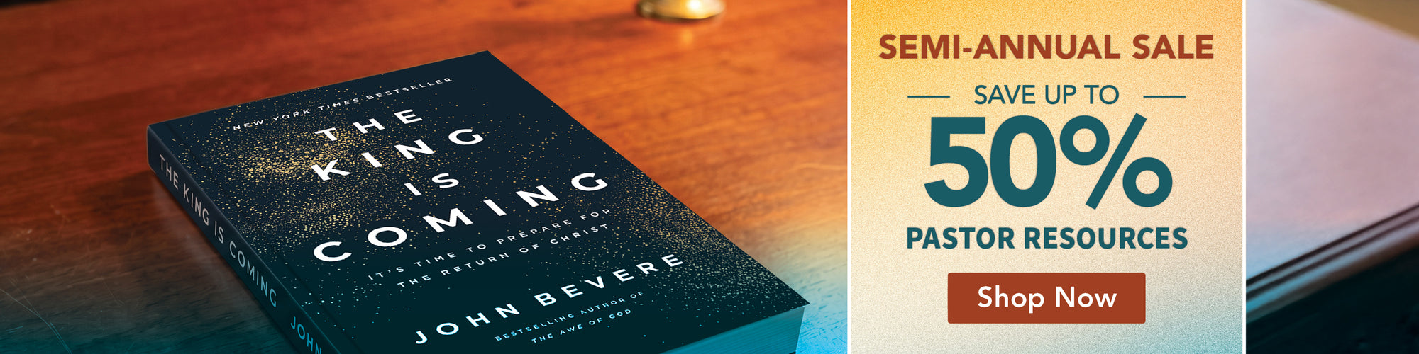 The King Is Coming paperback book by John Bevere displayed on a wooden table next to a promotional banner offering a 50% pastor resources sale.