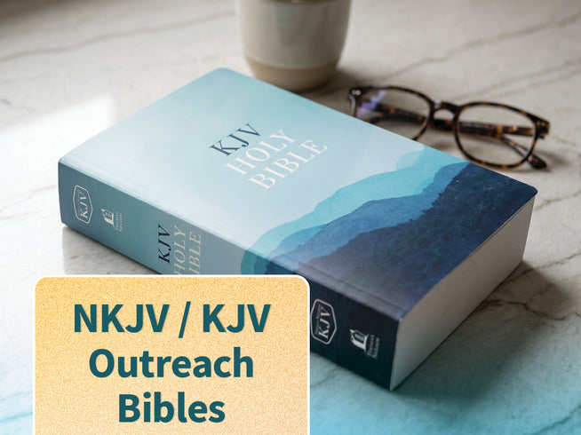 A KJV Holy Bible with a blue and teal landscape cover lies on a light marble surface, with a pair of eyeglasses and a cup in the background. A beige text box in the lower left reads 'NKJV / KJV Outreach Bibles'.