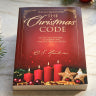 A hardcover book titled 'The Christmas Code' with a dark red cover, gold lettering, and a festive illustration of red and green Christmas candles at the bottom.
